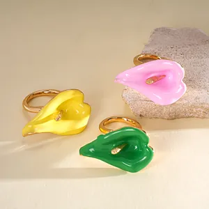 Detalle macro de tres anillos abiertos de flor de esmalte cala en amarillo, rosa y verde.