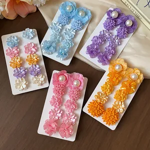Vista detallada de varios juegos de pendientes de flores y perlas en tarjetas blancas