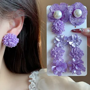 Detalle del set de pendientes de flores púrpuras y perlas en modelo y tarjeta exhibidora.