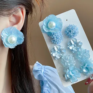 Vista macro de pendientes de flores azules con encaje, perlas y texturas variadas