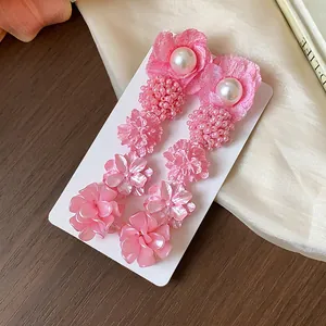 Primer plano de elegantes pendientes de flores rosas con perlas en tarjeta blanca