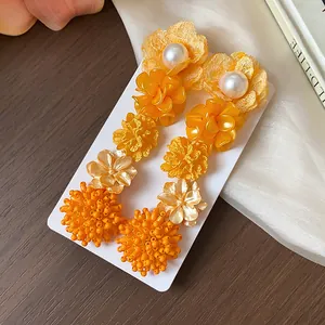 Detalle de pendientes florales naranjas con perlas y racimos de cuentas.