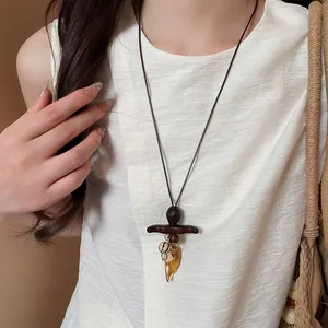 Detailed close-up of Bohemian style wooden resin pendant necklace worn on a white linen top