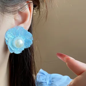 Detalle de primer plano de un pendiente de flor de tela azul con perla en la oreja.