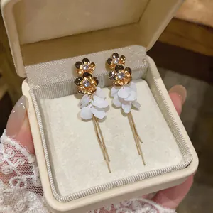 Detail of gold floral stud earrings with white resin petals and long tassels in a box