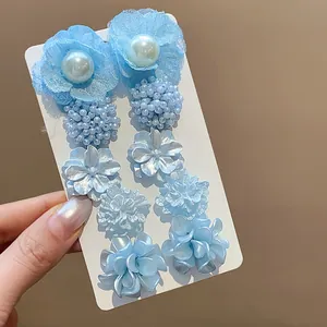 Primer plano de elegantes pendientes colgantes de flores de malla azul y perlas.