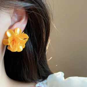 Detalle de un pendiente de flor naranja vibrante en la oreja de una modelo de moda