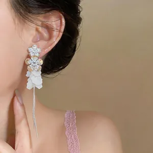 Close-up of elegant long tassel earrings with white resin petals and zircon flowers