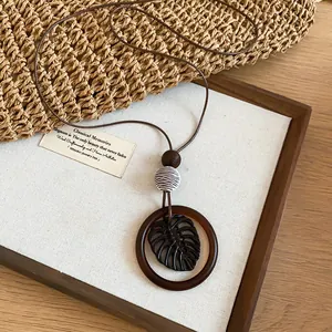 Detail view of a Bohemian monstera leaf pendant necklace on a rustic wooden display