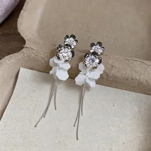 Close-up detail of silver zircon flower earrings with white resin petals and tassels
