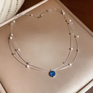 Detail view of a double-layered necklace with blue zircon pendant and pearls on a gold box