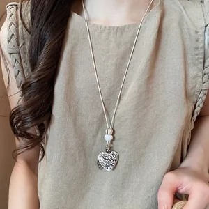 Detailed macro view of a bohemian vintage heart pendant necklace worn on a beige top