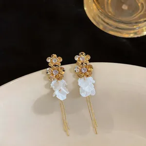 Detail showing golden flower zircon earrings with white resin petals and long tassels