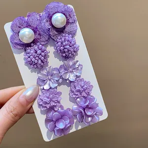 Primer plano detallado de pendientes de flores moradas con perlas en tarjeta blanca.