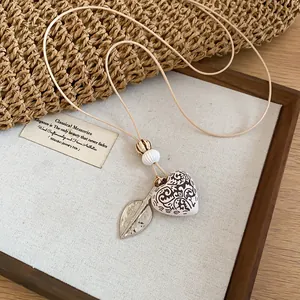 Close-up of Bohemian heart and leaf pendant necklace displayed on rustic wooden backdrop