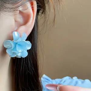 Elegante pendiente de flor azul claro con aguja de plata mostrado detalle en la oreja