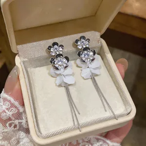 Detailed view of silver zircon flower earrings with white resin petals and chain tassels.