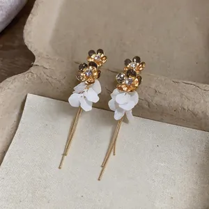 Macro detail view of gold flower earrings featuring white resin petals and elegant chain tassels