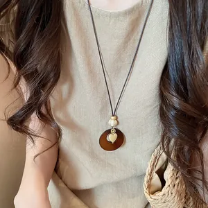 Close-up of Bohemian retro necklace with heart and circular pendant on beige top.
