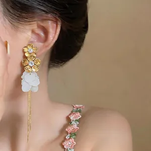 Detail view of zircon flower earrings with resin petals and long golden chain tassels