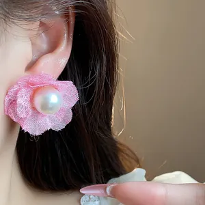Primer plano de un pendiente de flor de tela rosa con perla en la oreja