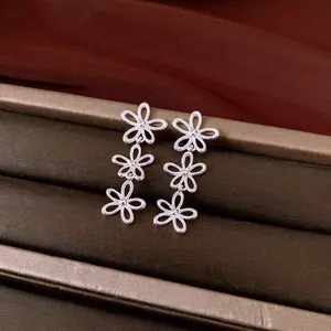 Elegant silver hollow flower dangle earrings displayed on a brown luxury jewelry tray.