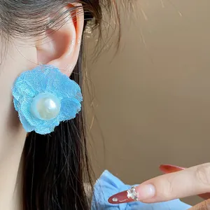 Primer plano de un pendiente de flor de encaje azul con perla en una oreja de mujer
