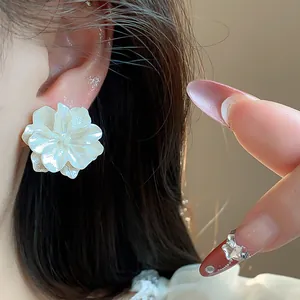 Primer plano de un pendiente de flor blanca nacarada en la oreja con elegante arte de uñas