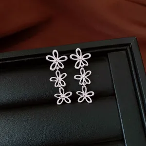 Close-up detail of silver-colored tiered hollow flower earrings on black display tray.
