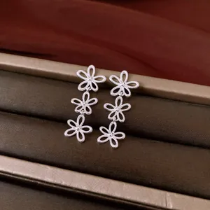 Detailed macro view of silver hollow flower drop earrings on a brown jewelry display tray.