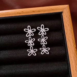 Detail view of silver hollow triple flower drop earrings on black velvet