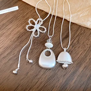 Detailed view of minimalist silver necklaces with zircon flower and bell pendants.