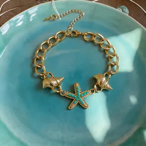 Dettaglio ravvicinato di un bracciale dorato con ciondoli stella marina e conchiglia