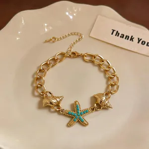 Dettaglio di bracciale a catena dorato con ciondoli a stella marina e conchiglie