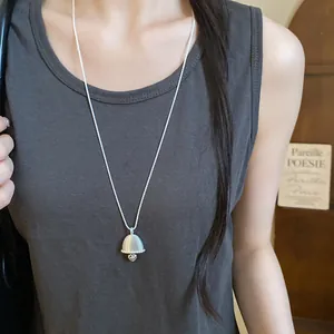Close-up of a minimalist silver bell pendant necklace with zircons on a model.