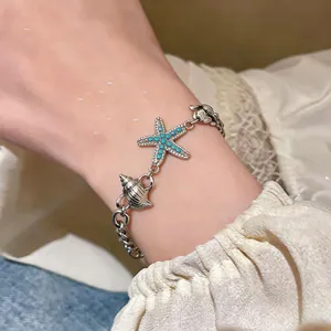 Primo piano di un bracciale in argento con ciondoli a stella marina, conchiglia e perline.