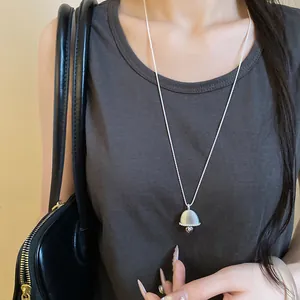 Close-up of a minimalist silver bell pendant necklace worn over a grey sleeveless top