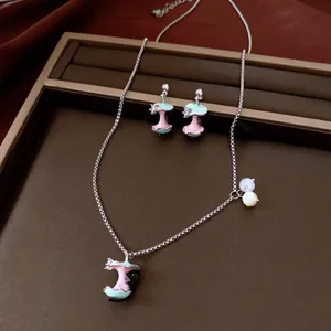 Detailed close-up view of the enamel cat and bitten apple core necklace and earrings jewelry set