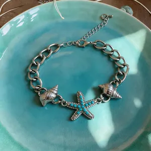 Dettaglio di un bracciale a catena argento con stella marina e conchiglie su piatto blu