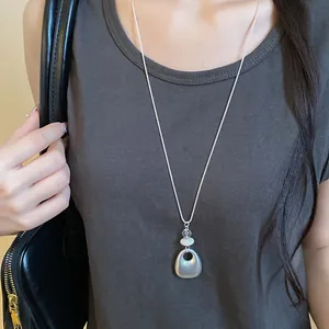 Model wearing a long silver-tone necklace with a geometric teardrop pendant over a grey top.