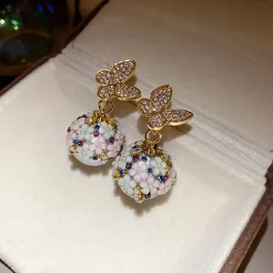 Detailed shot of gold butterfly earrings with floral rhinestone sphere pendants