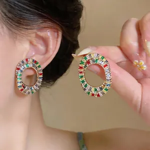 Detailed close-up of vibrant colorful zircon oval hollow earrings worn on ear and held in hand