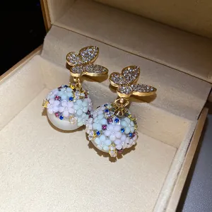 Detail of elegant earrings with butterfly and floral pearl motifs in a gift box.