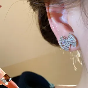 Detailed close-up view of elegant bow-shaped zircon stud earrings worn on a human ear
