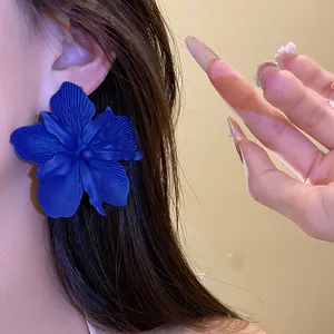 Close-up of large blue flower stud earring on ear showing matte spray-paint texture
