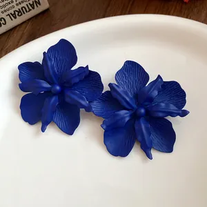 Close-up of matte blue flower earrings with detailed petal texture on a white plate