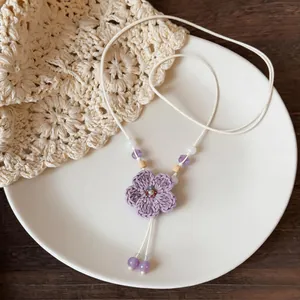 Detailed shot of a woven purple flower necklace with wood beads on a white plate