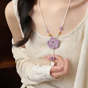 Close-up of a handmade purple woven flower necklace with ceramic beads on a model.