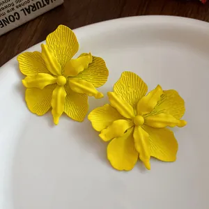 Detailed macro shot of yellow spray-painted floral stud earrings on a white ceramic plate