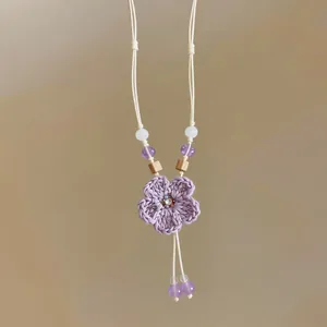 Close-up of a purple woven flower necklace with wood and purple beads on white cord